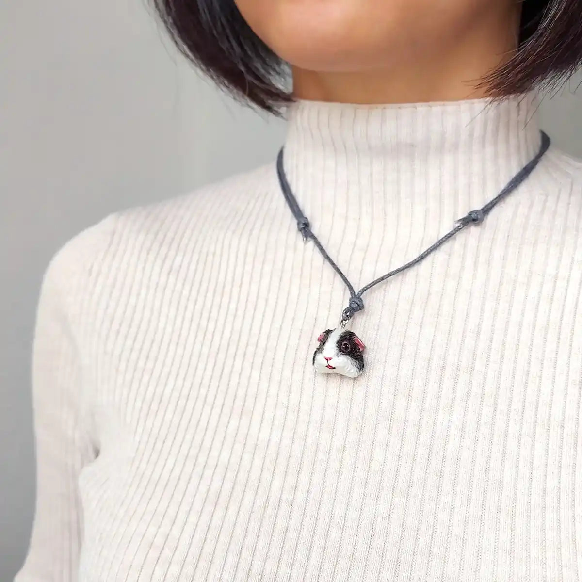 Hand-painted black and white American guinea pig pendant necklace on adjustable cotton cord wearing